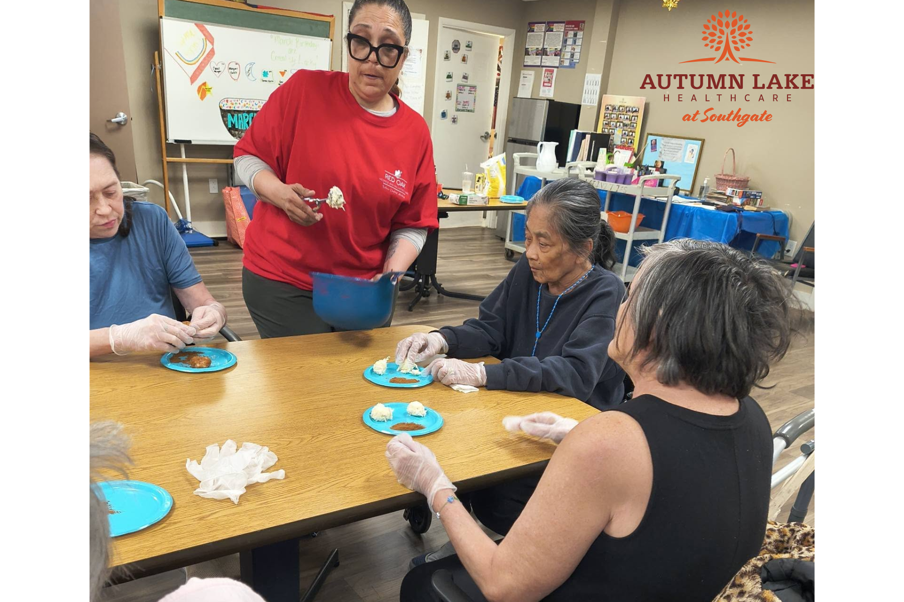 Residents at a rehabilitation care center participate in a hands-on food preparation activity at a communal table with a staff member.
