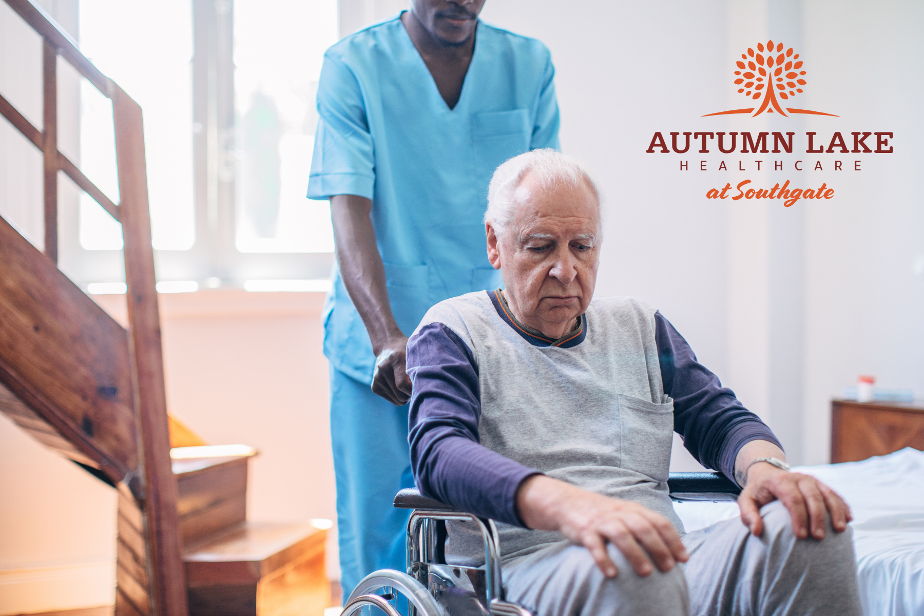 A male nurse in blue scrubs assisting an elderly man in a wheelchair at Autumn Lake Healthcare at Southgate.