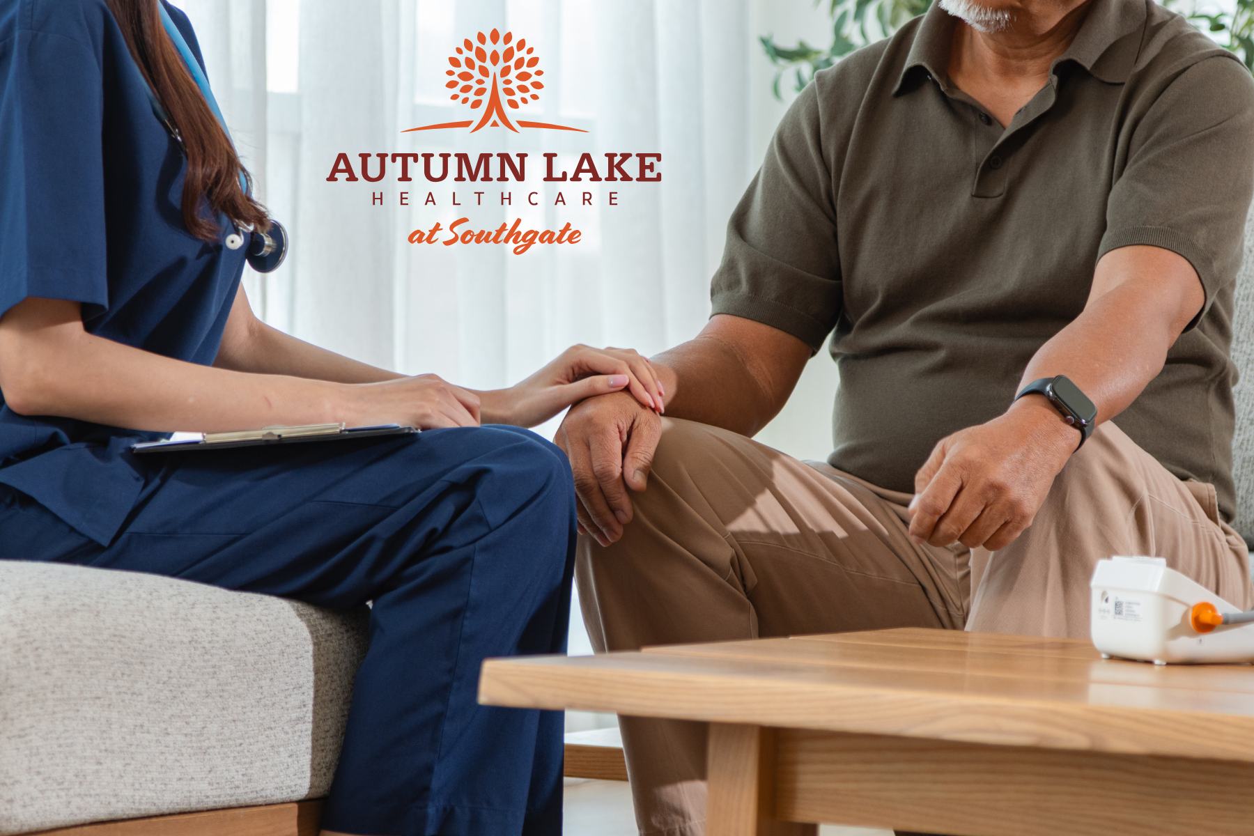 A nurse in blue scrubs gently places a hand on a male resident’s knee while conducting an assessment at Autumn Lake Healthcare at Southgate.